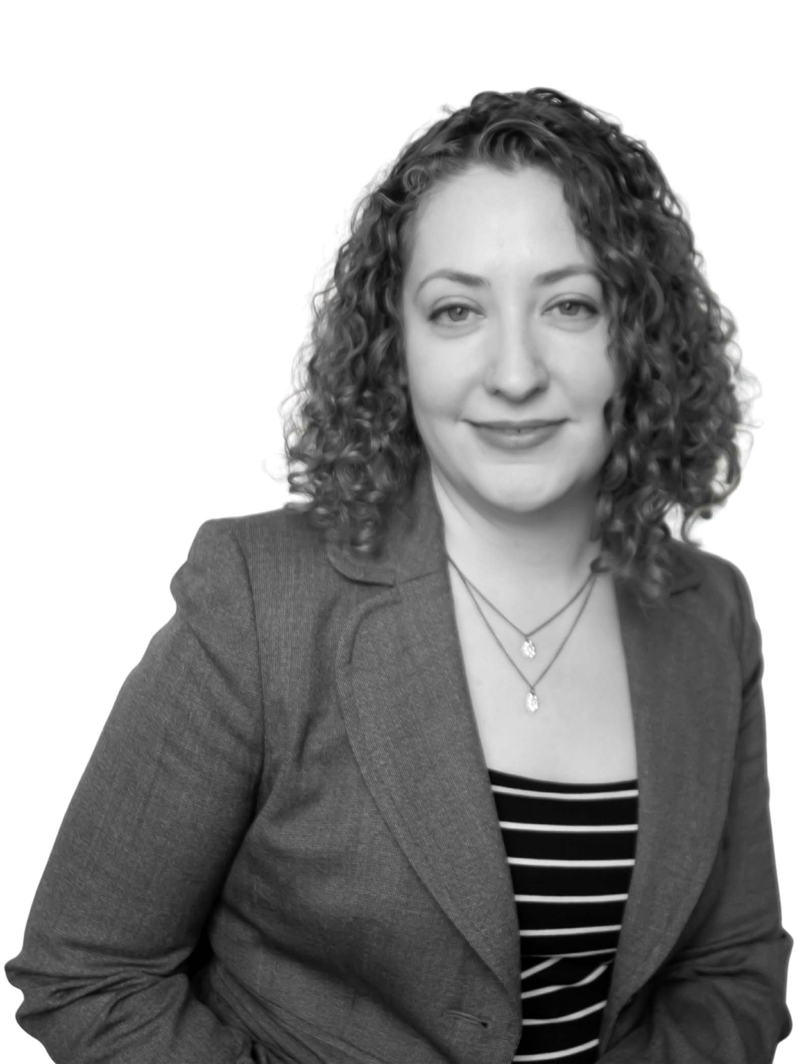 Black and white portrait of a woman with curly hair, wearing a blazer over a striped top and layered necklaces, smiling slightly while looking at the camera.