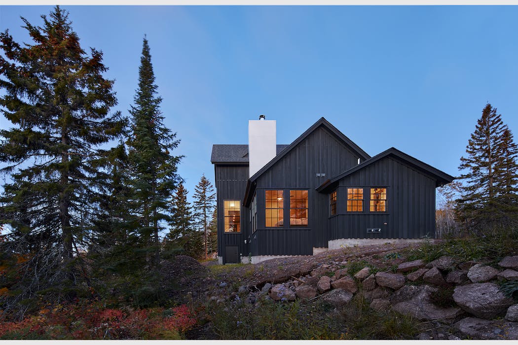 A modern, nordic inspired cabin by Albertsson Hansen Architecture sits besides tall trees in Tofte, Minnesota.