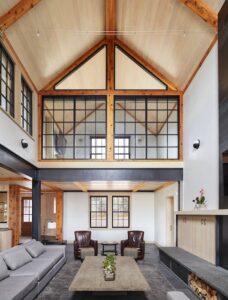 A living room with high A-Frame cielings, plush furniture and windows.