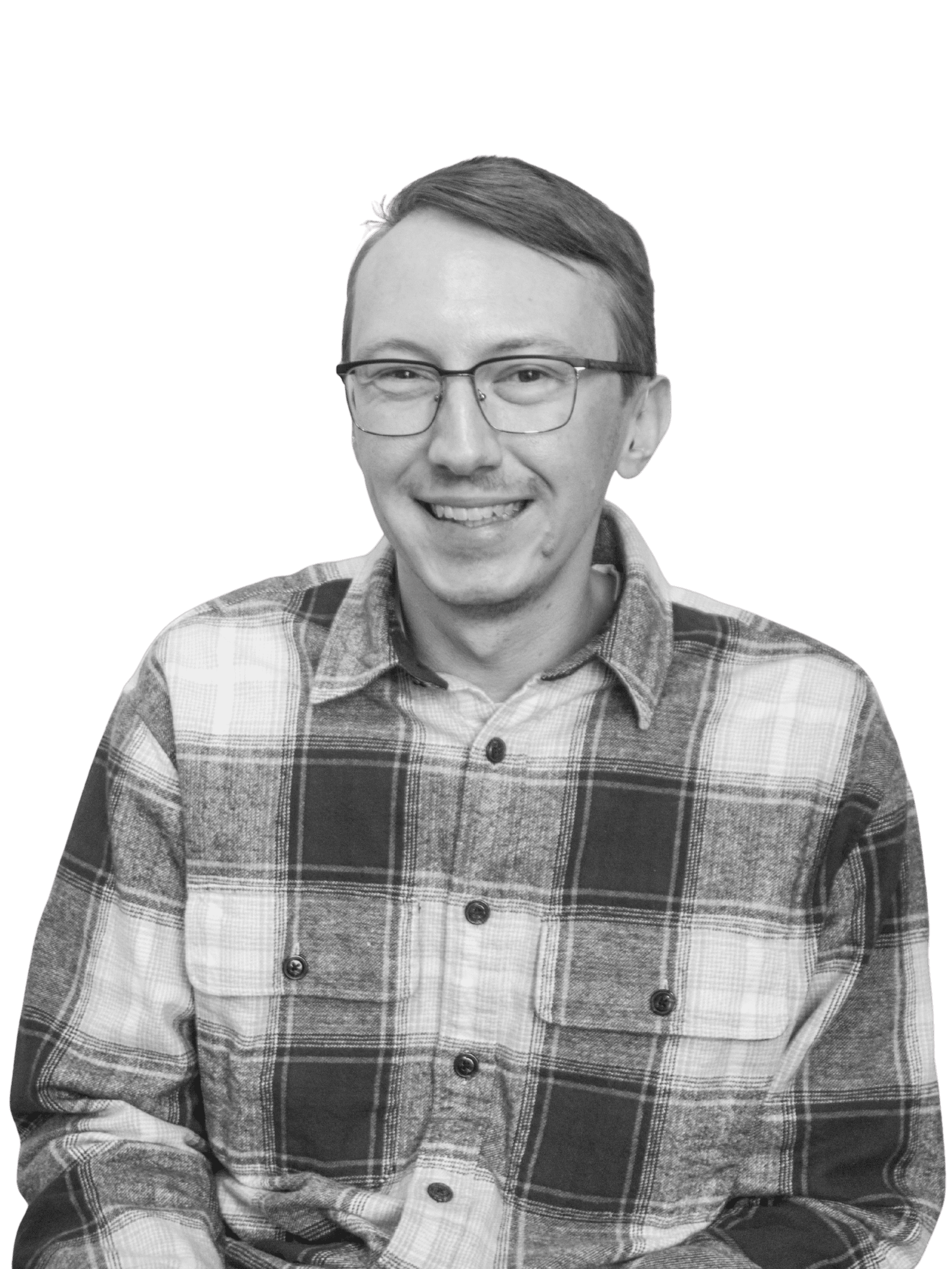 A man with short hair and glasses smiles at the camera. He is wearing a plaid button-up shirt. The background is plain white. This black-and-white photo features a Minnesota architect known for custom home design using natural materials.